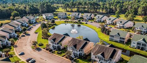 A residential area with houses, a central pond, and a golf course in the background.