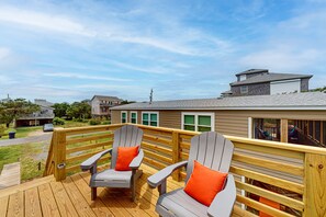 A deck with Adirondack chairs and a wooden railing overlooking a residential area.