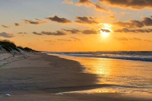 Ein Strand mit Sonnenuntergang, Wellen und Dünen.