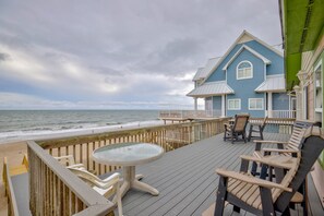 Une terrasse en bois avec une table et des chaises en verre, offrant une vue sur l’océan.
