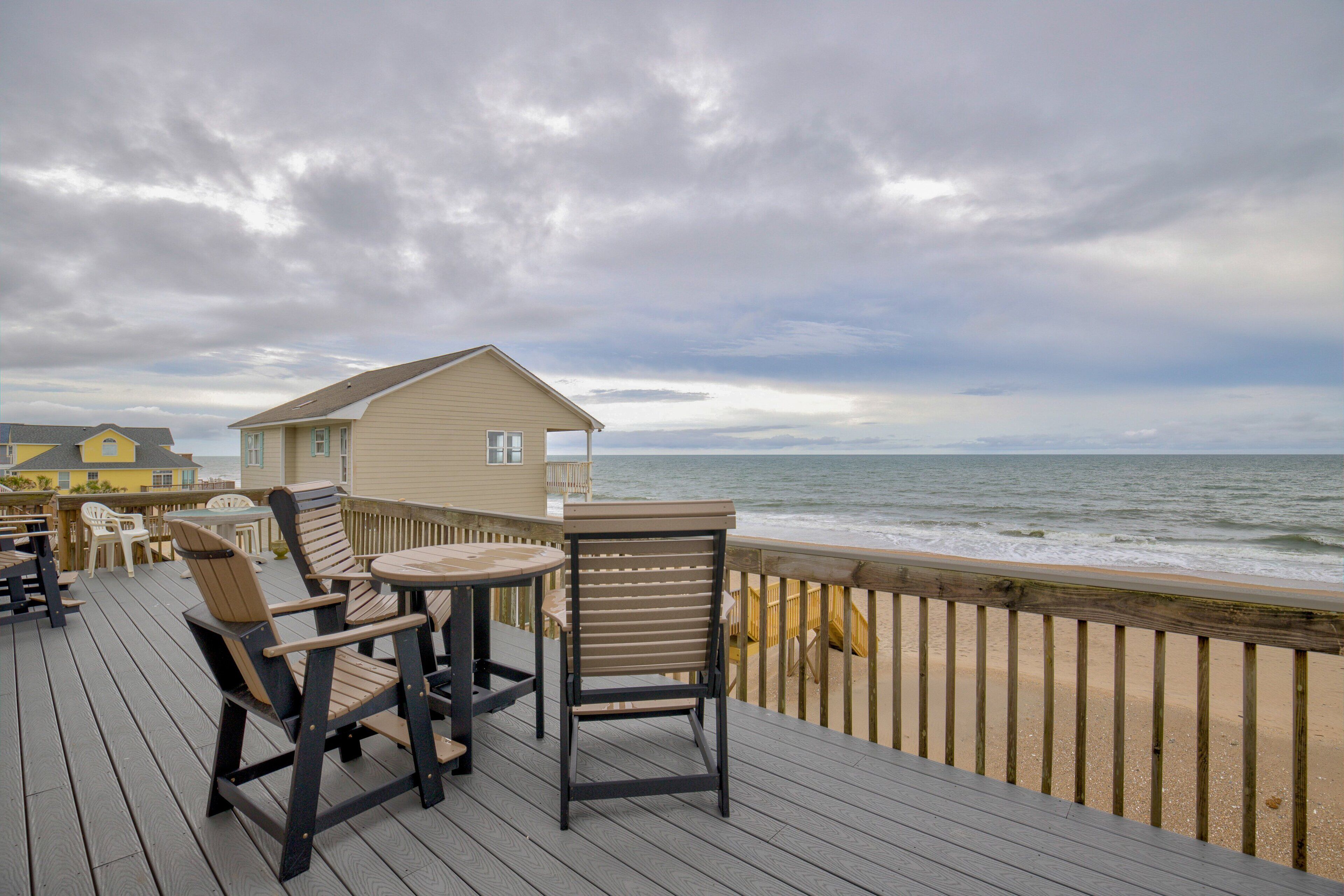 A wooden deck with outdoor furniture, a beach view, and a building in the background.