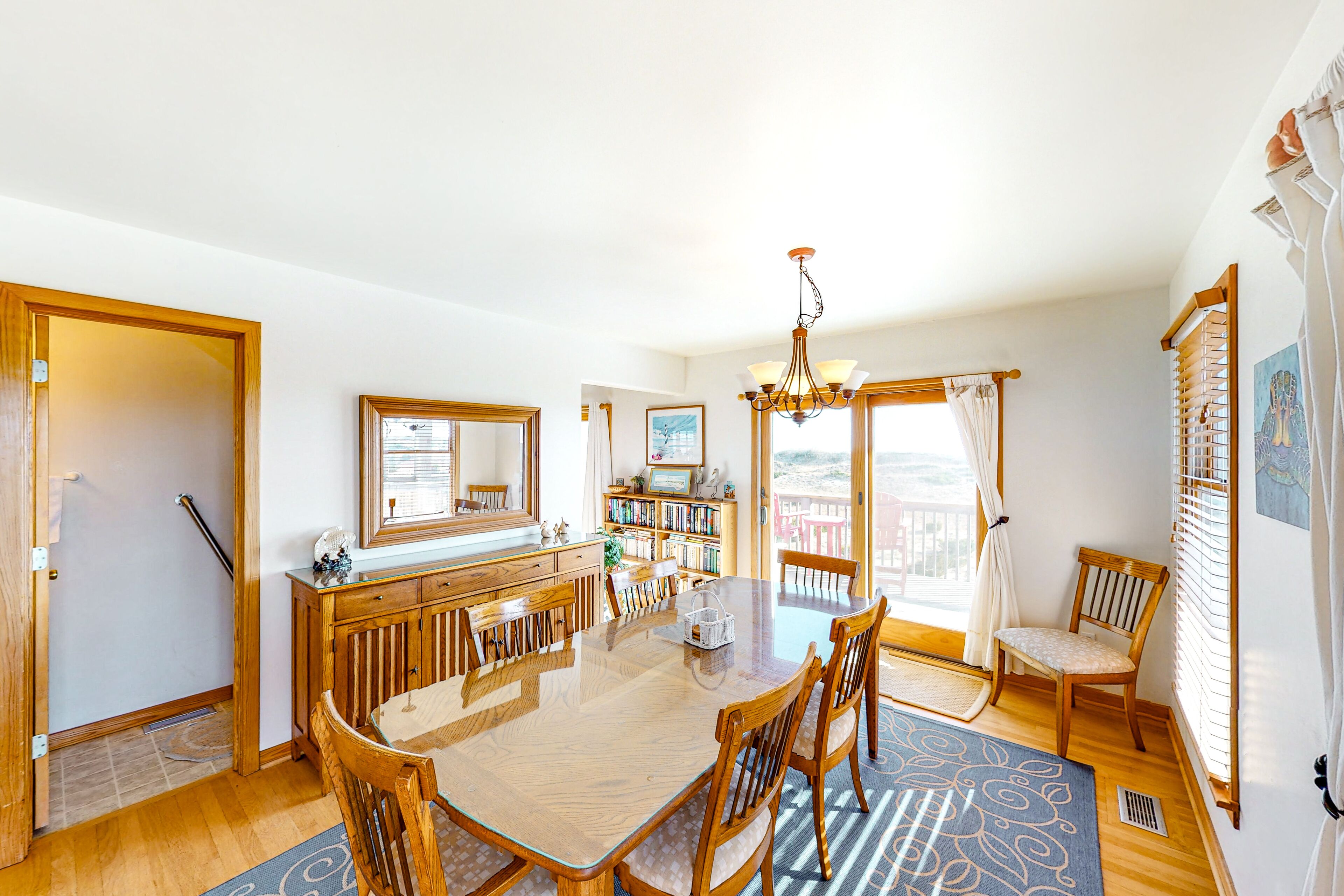A spacious dining area with a wooden table and chairs, a bookshelf, and a view of the outdoors.
