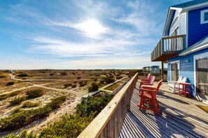 A wooden deck with red chairs and a blue building with a balcony overlooking a beach landscape. - Oceanfront house w/private washer/dryer, hot tub, WiFi, central AC, & balcony (Salvo)
