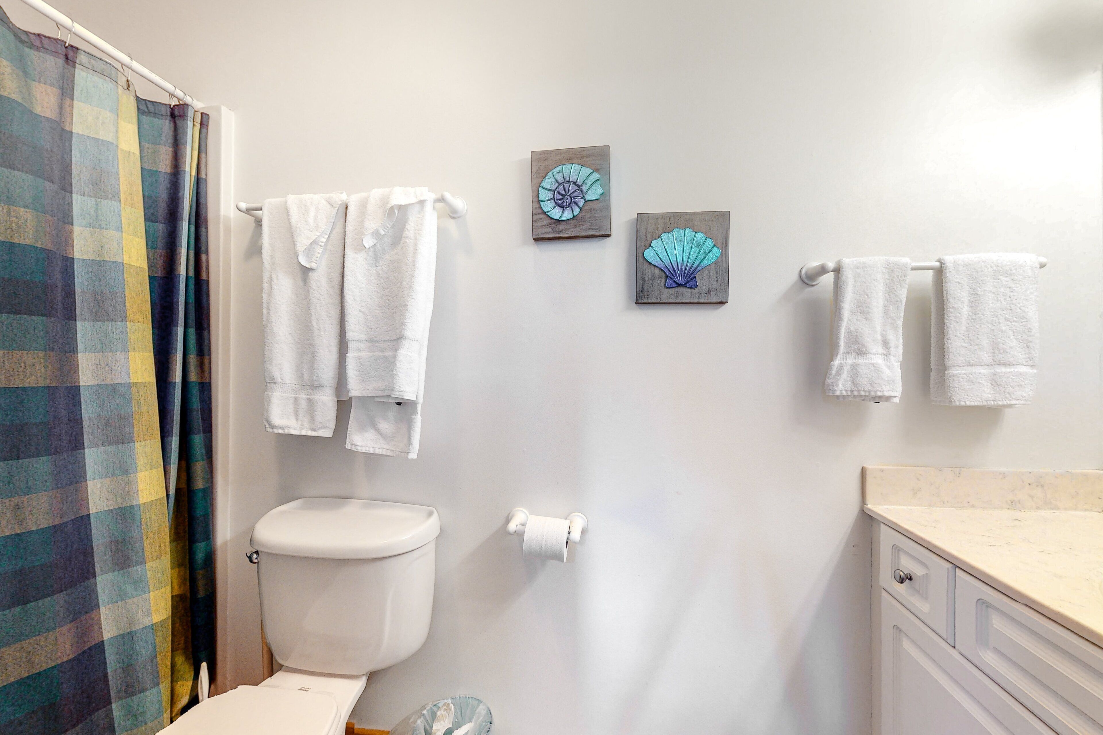 Une salle de bain avec des toilettes, deux serviettes accrochées au mur et un rideau de douche.