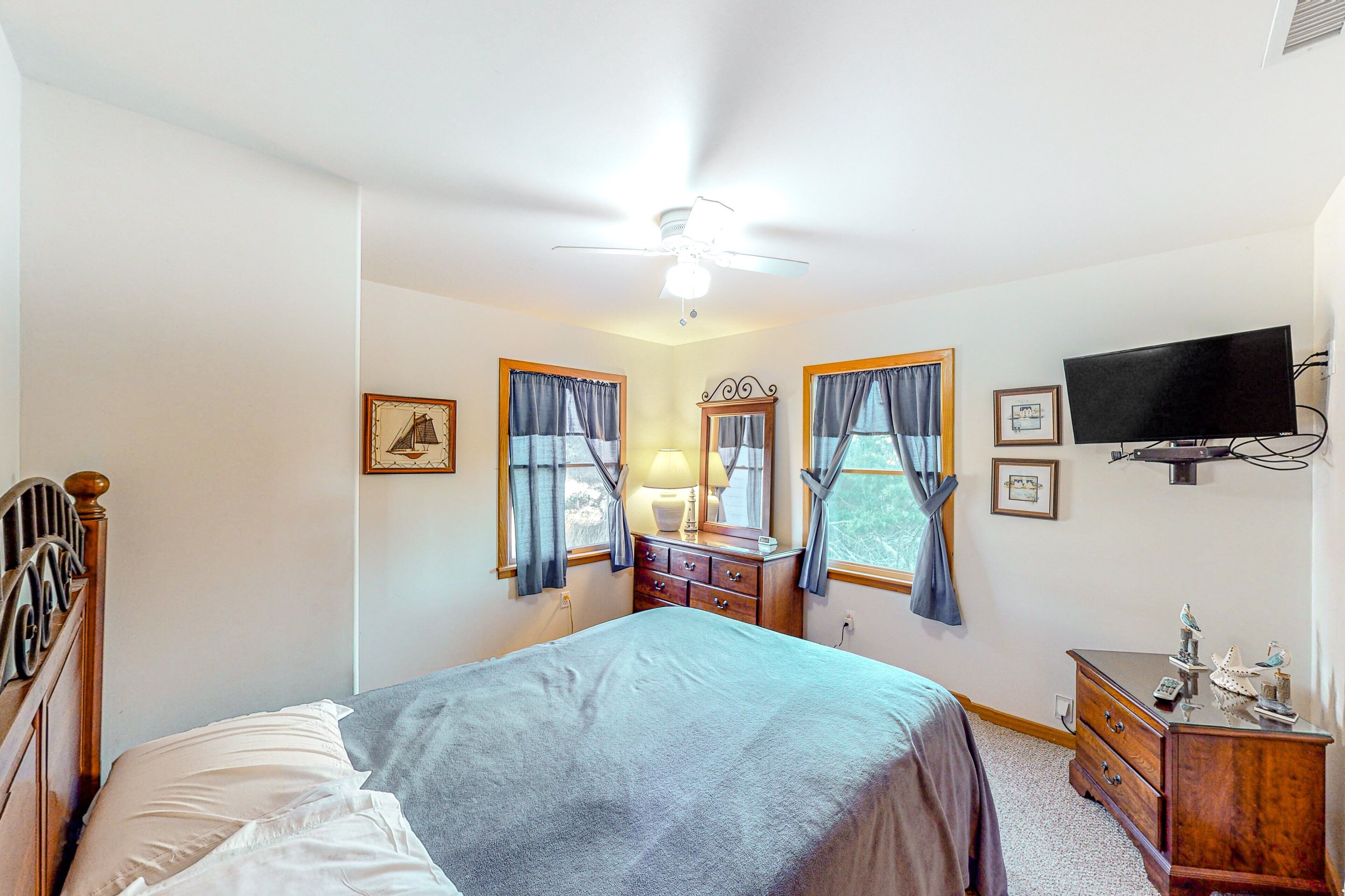 A bedroom with a bed, dresser, vanity, and a ceiling fan.