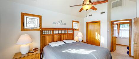 A bedroom with a wooden headboard, two bedside tables with lamps, a ceiling fan, and a door leading to another room.