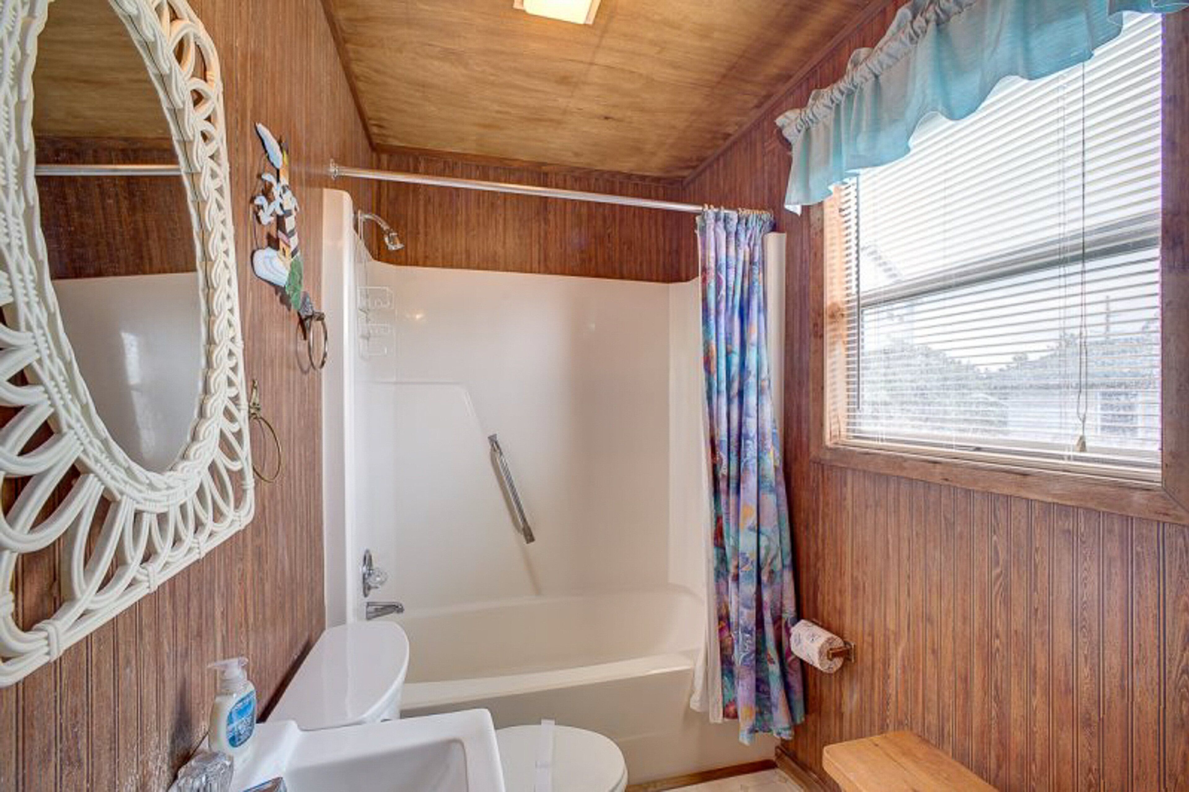 A bathroom with a wooden interior, a bathtub, a sink, a mirror, and a window with blinds.