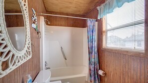 Un bagno con arredi in legno, una vasca, un lavandino, uno specchio e una finestra con persiane.