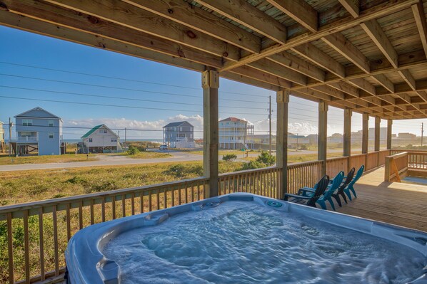 A wooden deck with a hot tub and chairs, overlooking a road and houses.