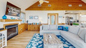 Ein geräumiges Wohnzimmer mit Kamin, einer großen Couch und einem Deckenventilator.