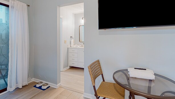 Ein Zimmer mit Glastisch, Korbstuhl und einem an der Wand befestigten Fernseher.