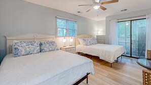 Ein Schlafzimmer mit zwei Betten, einem Deckenventilator und einer Schiebetür zu einem Außenbereich.