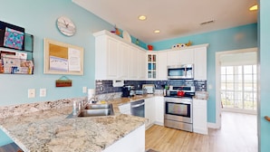 A kitchen with white cabinets, a granite countertop, stainless steel appliances, and a window to the right. - Oceanfront duplex with 4 decks, private beach walkway, central AC, & W/D (North Topsail Beach)