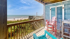A wooden deck with a view of the beach, a blue building with a door, and two pink chairs. - Oceanfront duplex with 4 decks, private beach walkway, central AC, & W/D (North Topsail Beach)