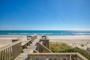 A wooden boardwalk leading to a beach with a clear view of the ocean.