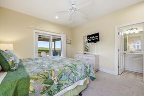 A bedroom with a bed, a ceiling fan, a TV, a dresser, and a bathroom door. - Oceanfront home with ocean view, private hot tub & pool, & washer/dryer (Hatteras)