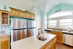A kitchen with stainless steel appliances, wooden cabinets, and a large window providing natural light.