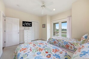 A bedroom with two beds, a ceiling fan, a TV on the wall, and a view of the outdoors through a sliding door.