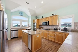 A modern kitchen with wooden cabinets, stainless steel appliances, and a large island. - Oceanfront home with ocean view, private hot tub & pool, & washer/dryer (Hatteras)