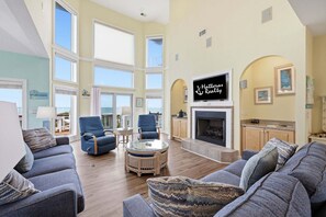 A spacious living room with a fireplace, large windows, and a view of the ocean.