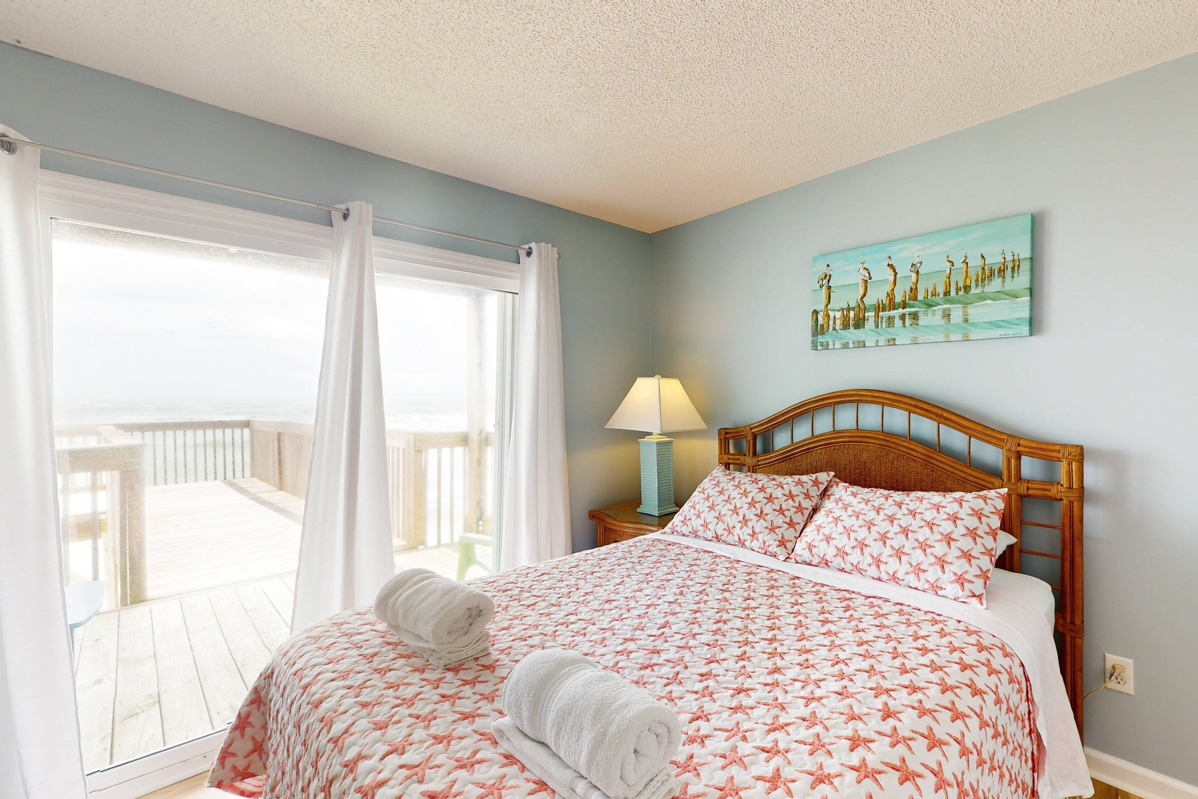 A bedroom with a bed, a nightstand, a lamp, a painting, and a view of a balcony.
