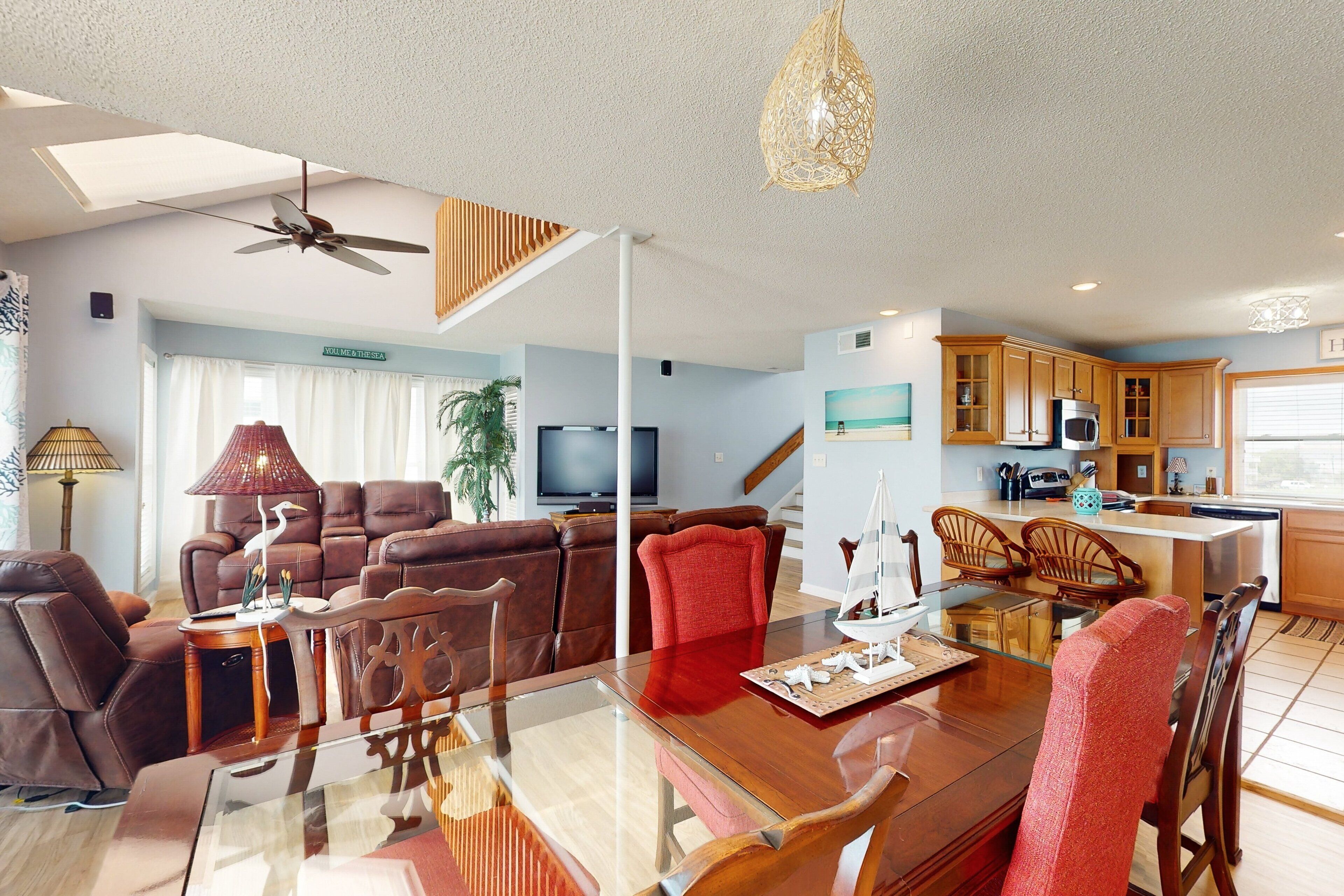 A spacious living room with a glass dining table, leather sofas, and a kitchen area with wooden cabinets.