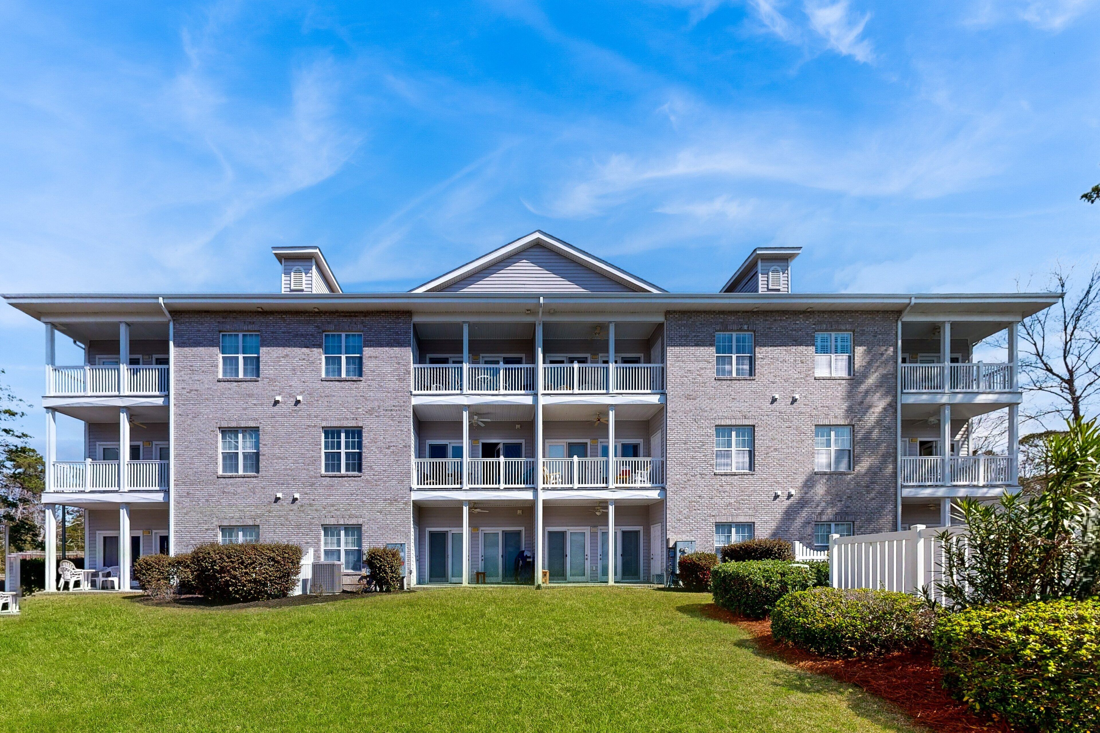 A multi-story building with a symmetrical facade, balconies, and a well-maintained lawn.