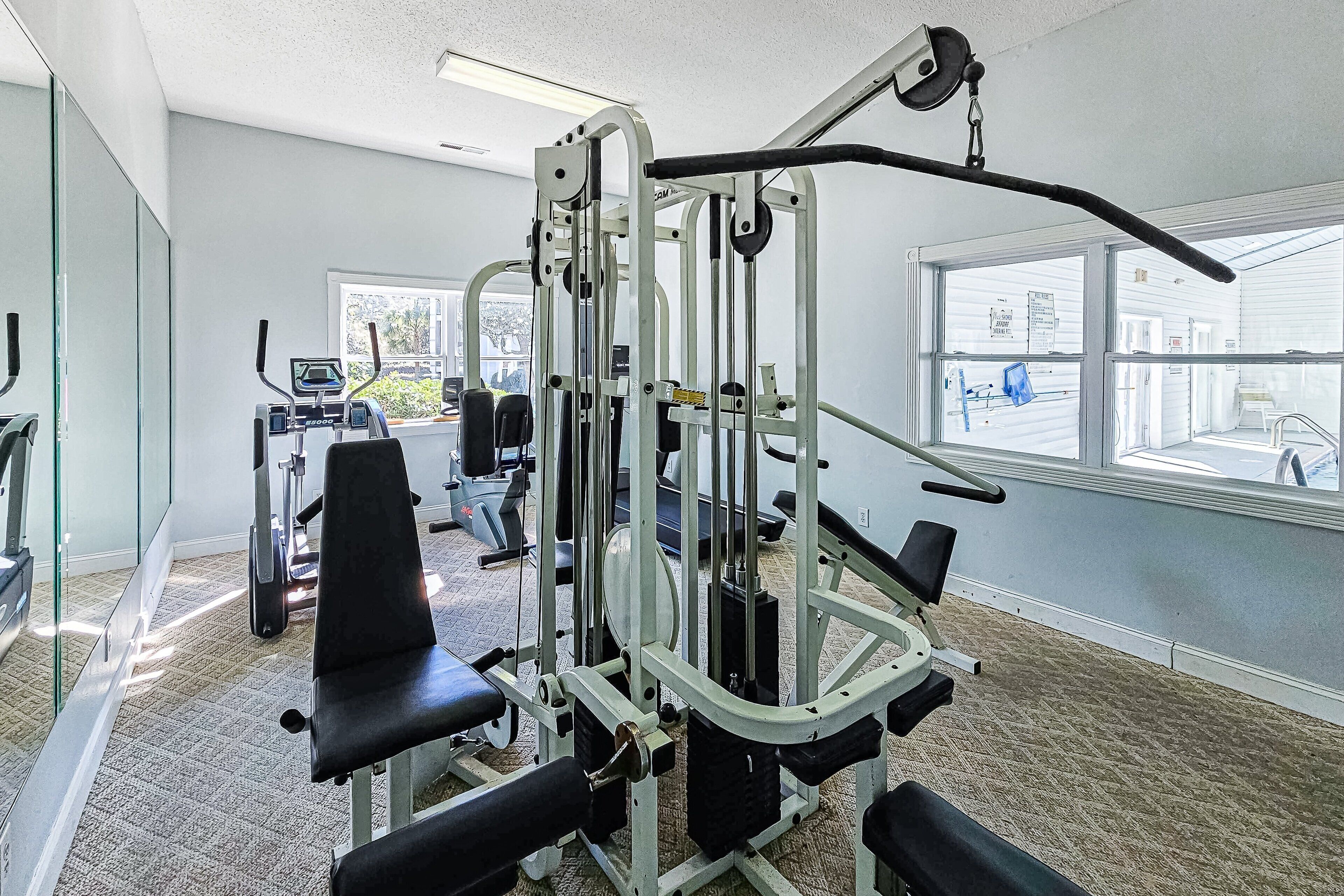 Uma academia com equipamentos de ginástica, esteira e uma janela com vista para o exterior.