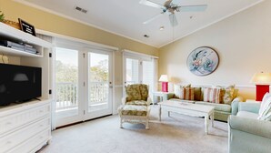 Un salon spacieux comprenant un meuble de rangement blanc pour l’équipement audiovisuel, un téléviseur, un ventilateur de plafond, un ensemble de canapés et une table basse.