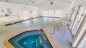Une piscine intérieure avec un plongeoir, un espace détente avec une table et des chaises, et une porte portant l’inscription « Sortie ».
