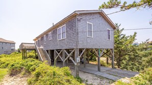 Une maison à deux étages dotée d’une terrasse en bois et d’un escalier menant à un porche abrité.