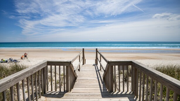 A wooden boardwalk leading to a beach with clear skies and calm sea.