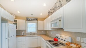 A kitchen with white cabinets, a stove, a microwave, and a sign that reads "BEACH HOUSE". - Ocean view duplex with a washer/dryer, central AC, deck, & golf nearby (North Topsail Beach)