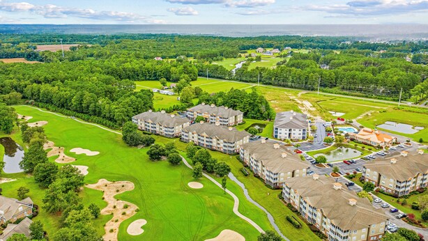 A golf course with bunkers and a clubhouse. There are multiple buildings with a uniform architectural style. - Crow Creek Retreat: Golf-course-front villa at Crow Creek with screened porch and washer/dryer (Calabash)