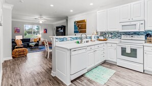 A modern kitchen with white cabinetry, a blue and white backsplash, and a central island. - Crow Creek Retreat: Golf-course-front villa at Crow Creek with screened porch and washer/dryer (Calabash)