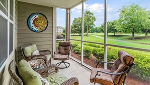 A covered porch with wicker furniture, a sun decoration, and a view of a golf course. - Crow Creek Retreat: Golf-course-front villa at Crow Creek with screened porch and washer/dryer (Calabash)
