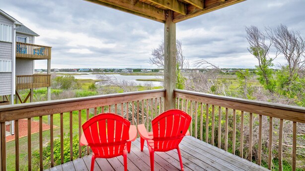 A wooden deck with two red chairs facing a view of a lake and surrounding greenery. - Water-view two-story duplex with multiple decks, outdoor shower, washer/dryer (North Topsail Beach)