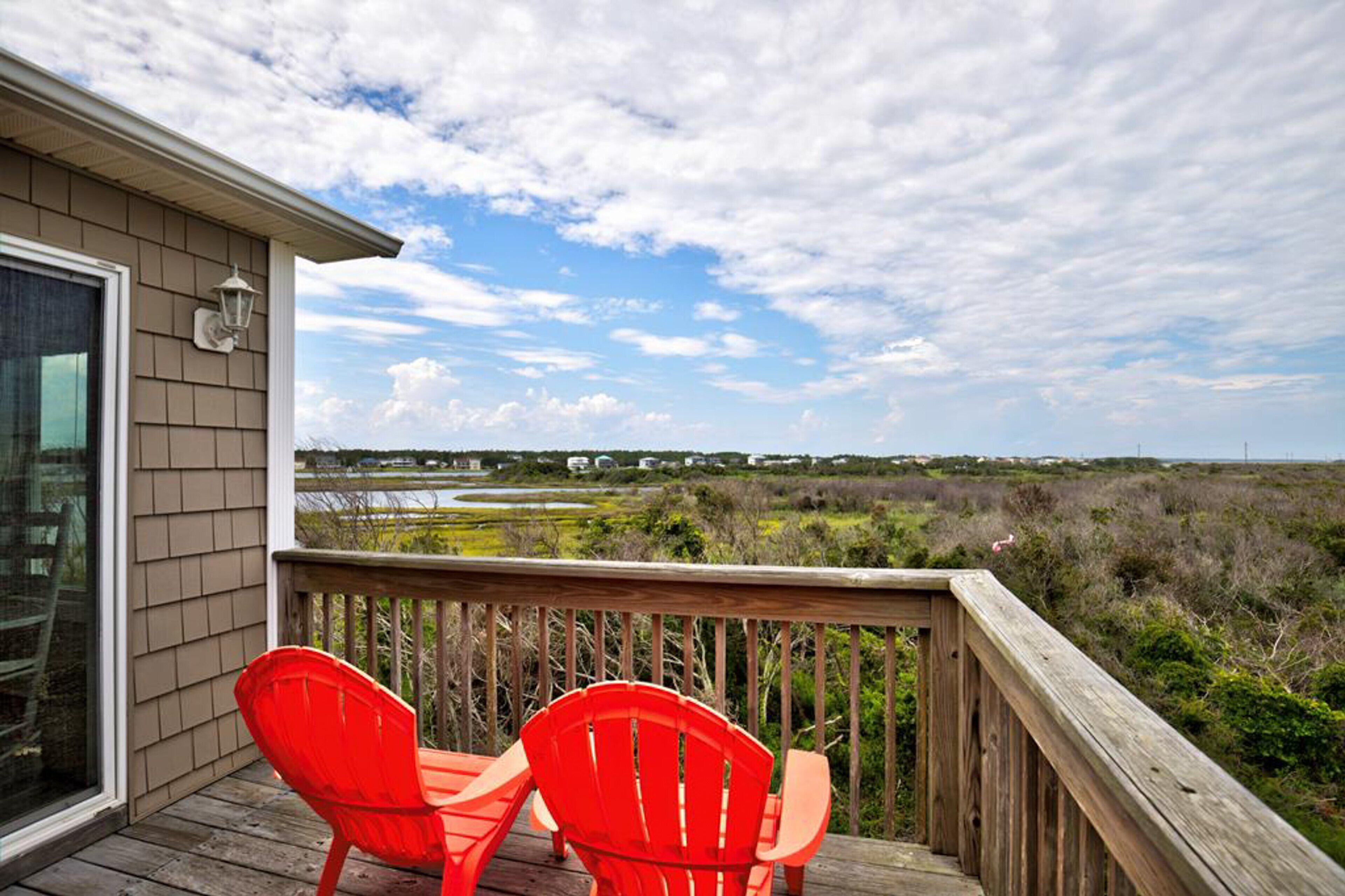 A wooden deck with two red chairs overlooking a coastal landscape.