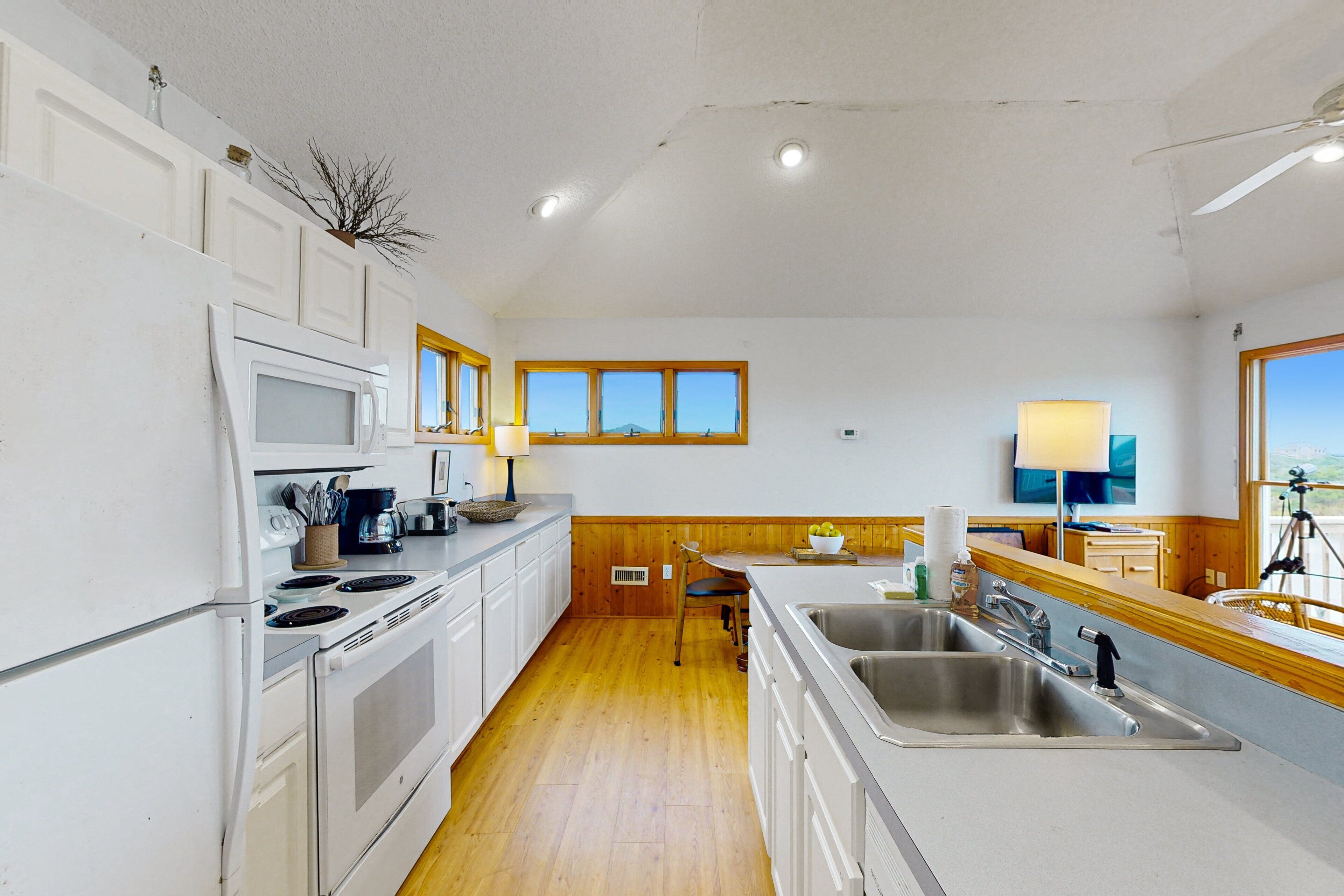 Une cuisine avec des meubles blancs, une cuisinière, un four à micro-ondes, un évier et un plancher en bois.