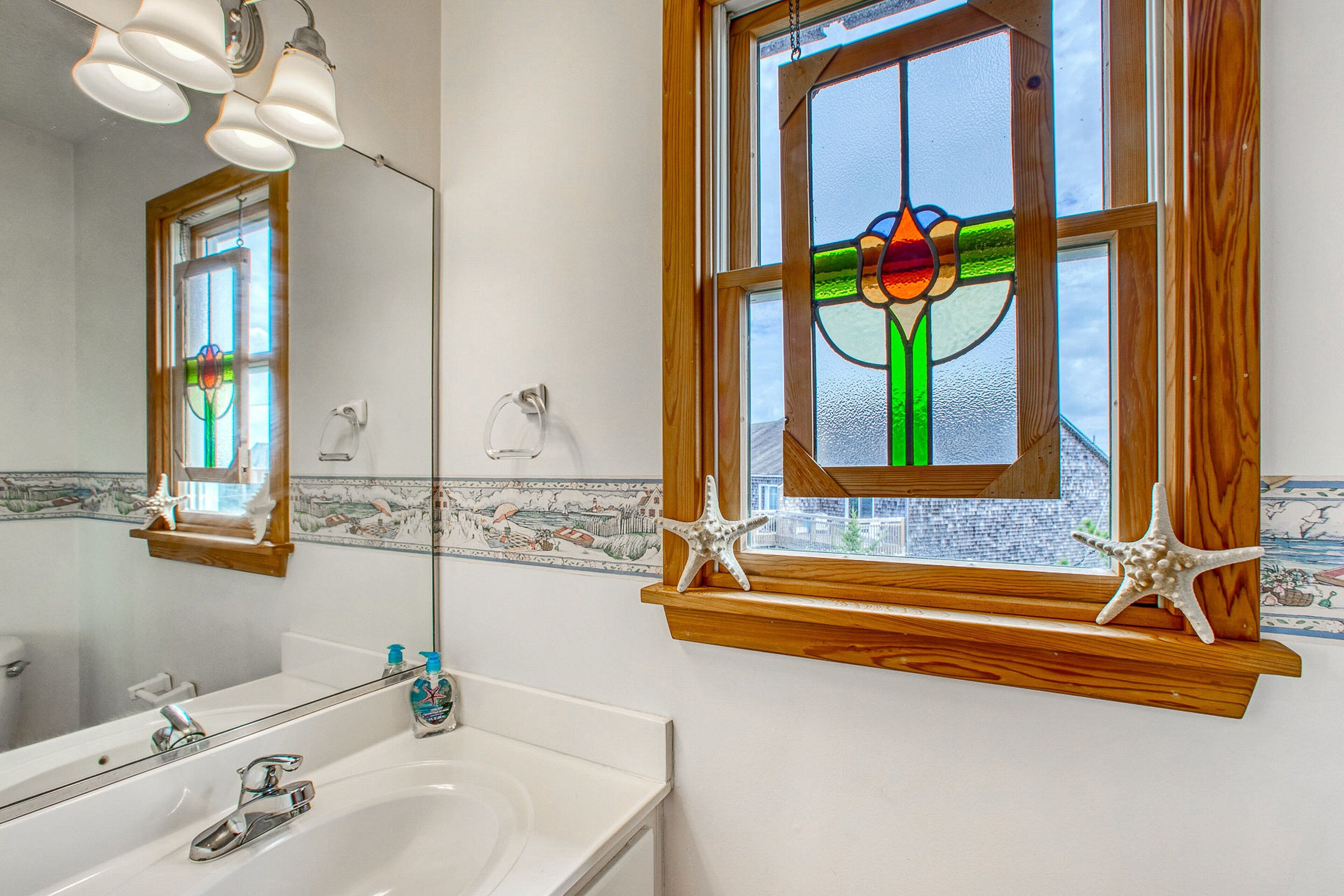 A bathroom with a white sink, a mirror, and a stained glass window above the sink.