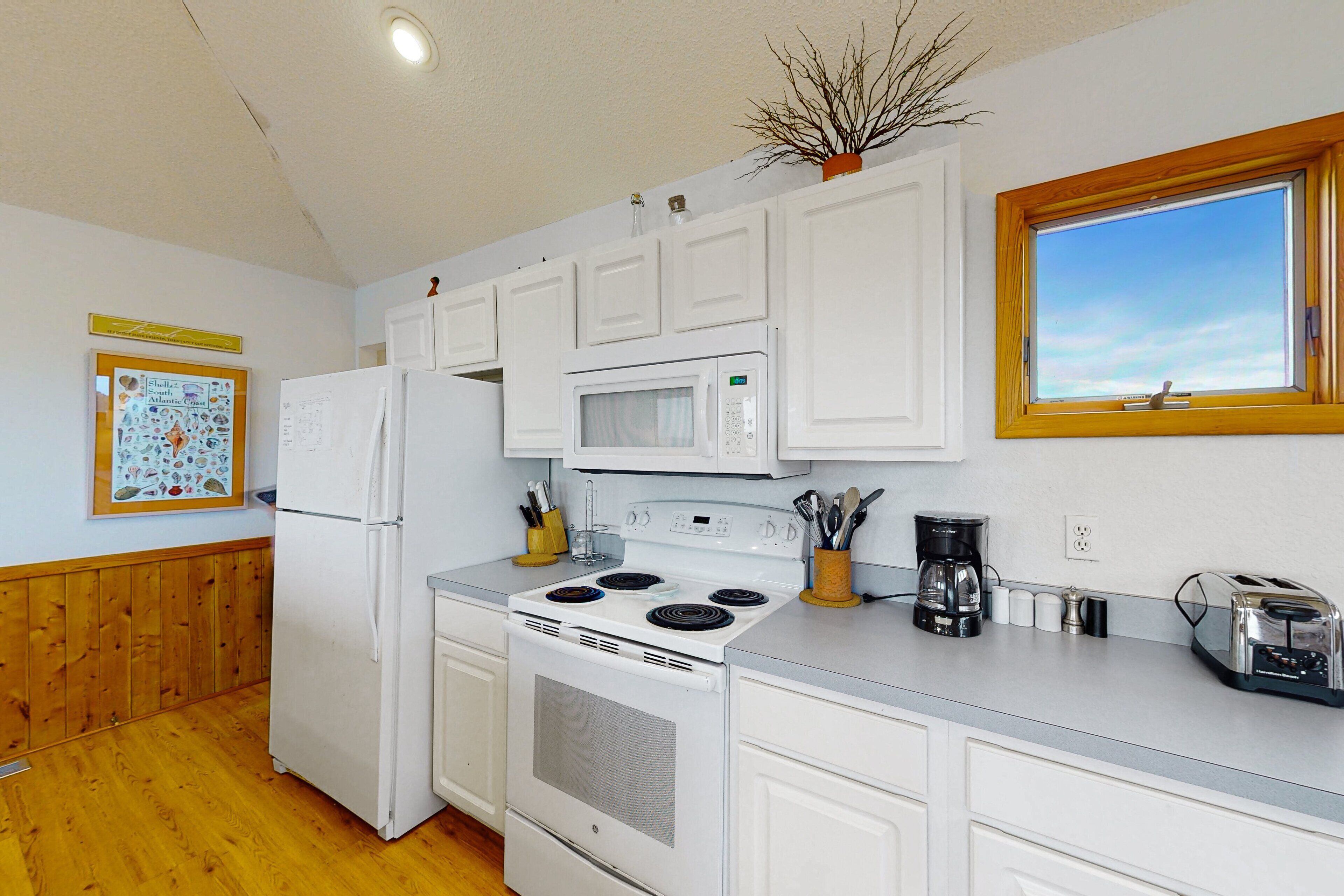 A kitchen with white cabinets, a refrigerator, a stove, and a microwave. There is a window with a view of the sky.
