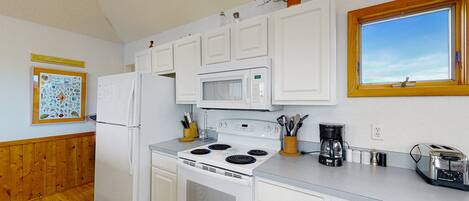 A kitchen with white cabinets, a refrigerator, a stove, and a microwave. There is a window with a view of the sky.