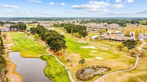 Vue aérienne d’un terrain de golf avec un étang, entouré de bâtiments résidentiels et d’arbres.