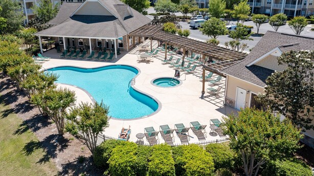 Un espace piscine avec des chaises longues et un coin salon abrité, entouré d’arbres et d’immeubles.