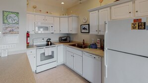 A kitchen with white cabinets, a microwave, a toaster, a sink, and a refrigerator. - Oceanfront, dog-friendly condo with ocean view, central AC & WiFi (Hatteras)