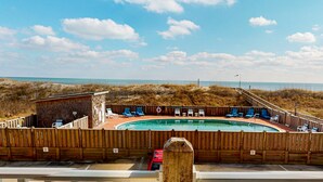A pool area with a wooden fence, lounge chairs, and a view of the beach and ocean. - Oceanfront, dog-friendly condo with ocean view, central AC & WiFi (Hatteras)