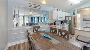Una cocina moderna con gabinetes blancos, un refrigerador de acero inoxidable y un comedor con mesa y sillas.