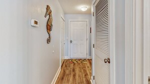 Un pasillo estrecho con suelo de madera, una puerta blanca al final y un termostato en la pared.