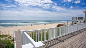 Ein Holzdeck mit weißen Geländern, das auf einen Strand mit blauem Himmel blickt.