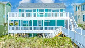 Ein zweistöckiges Strandhaus mit Balkon und einer Treppe, die zum Obergeschoss führt.